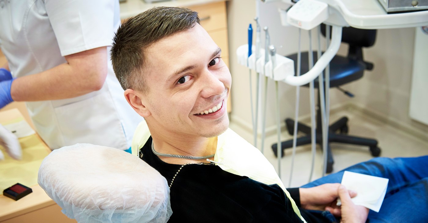 Paciente adulto joven sonriendo en el sillón de la clínica dental