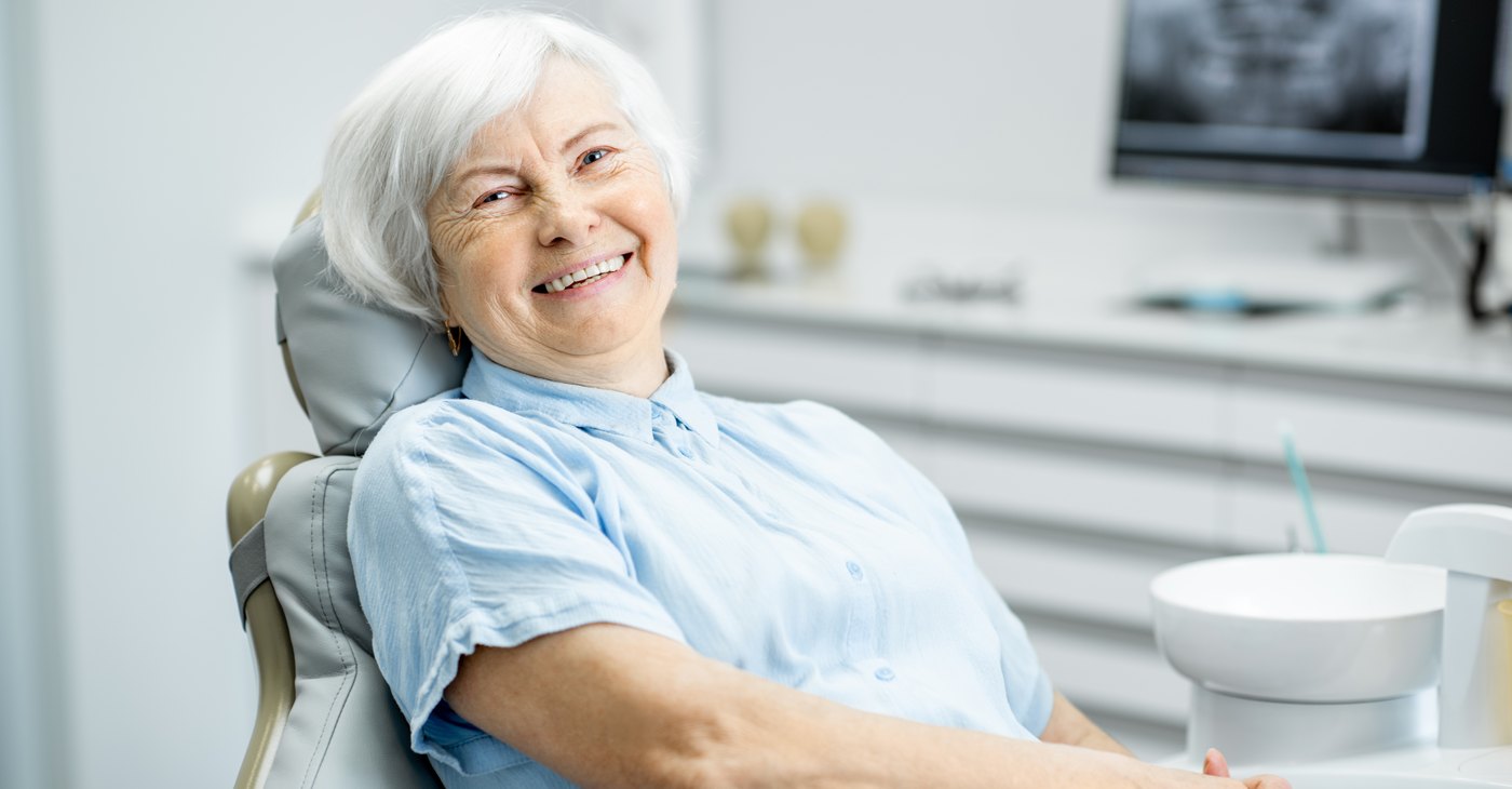 Older patient smiling in the dental chair years after her implant treatment