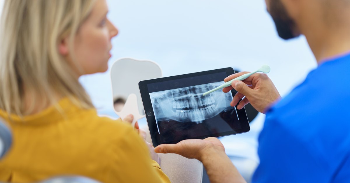 Cuánto dura un implante dental: el dentista muestra a su paciente una radiografía panorámica en una tableta durante la revisión