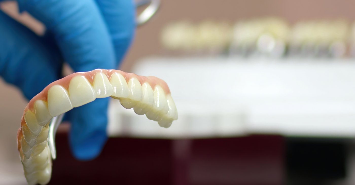 Arcada completa de porcelana terminada en el laboratorio dental, sostenida con guante