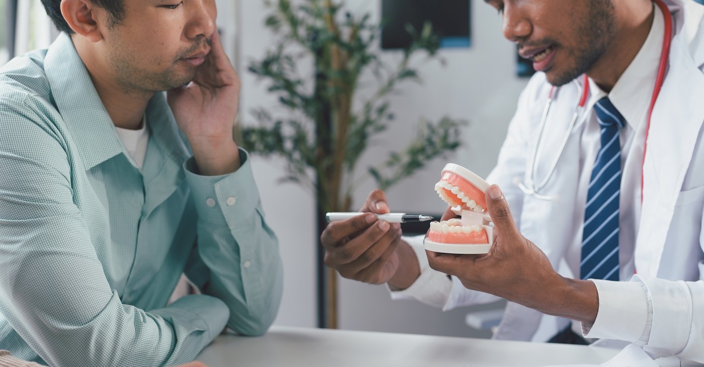 El dentista explica al paciente cómo afecta el tabaco con un modelo dental en la mano