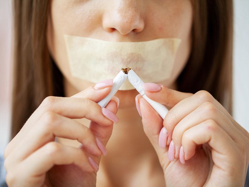 Mujer partiendo un cigarrillo por la mitad, con la boca tapada con cinta