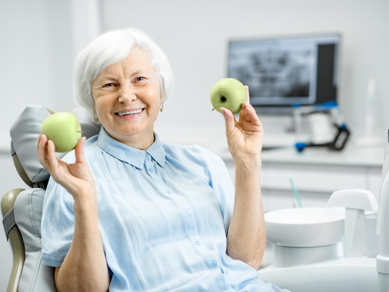 Mujer mayor sonriente en el sillón del dentista con una manzana en cada mano