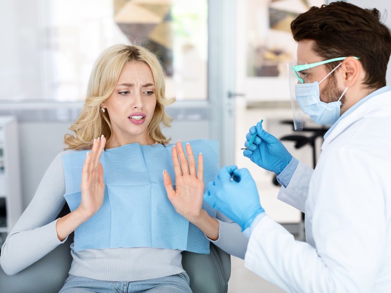 Paciente en el sillón dental levantando las manos con gesto de miedo ante el dentista
