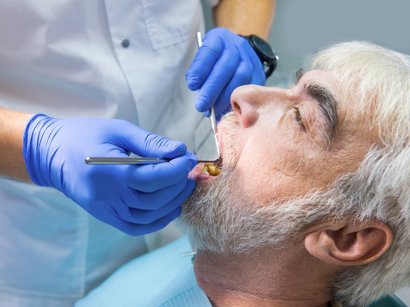 Dentista explorando la boca de un hombre mayor con espejo y sonda